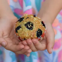 Dziecko trzyma w dłoniach pyszne muffinki z borówkami mrożonymi, posypane chrupiącym ziarnem.