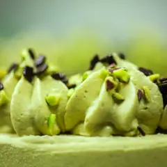 Delikatna beza z kremem pistacjowym, ozdobiona posiekanymi pistacjami i czekoladą.