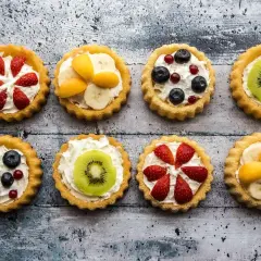 Kolorowe tartaletki z owocami: truskawki, kiwi, borówki, maliny i morele na kremowym nadzieniu.