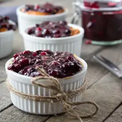 Słodki pomysł na deser: frużelina malinowa w białych kokilkach, obok słoik z przetworami i nożyczki.
