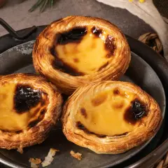 Trzy pyszne portugalskie ciastka, znane jako pastéis de nata, z chrupiącym ciastem i kremowym, lekko przypieczonym nadzieniem.