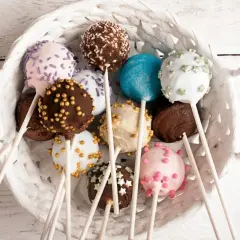 Kolorowe cake pops kokosowe w białym koszyku, udekorowane posypkami i kuleczkami.
