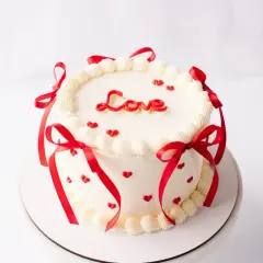 Biały tort z napisem "Love", ozdobiony czerwonymi serduszkami i wstążkami. Idealny na Walentynki, jako inspiracja do bento przepis.