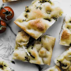 Pyszna focaccia z ziołami i parmezanem, idealna do przygotowania według prostego przepisu. Obok gałązka pomidorków koktajlowych.