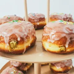 Pyszne pączki pistacjowe z lukrem i kolorową posypką, ułożone na paterze.