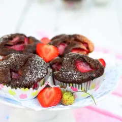 Pyszne muffiny czekoladowe z truskawkami, posypane cukrem pudrem, prezentują się apetycznie na talerzyku.