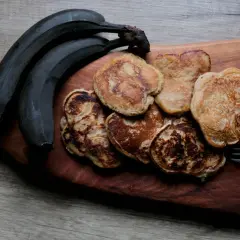 Placki bananowe z masłem orzechowym, obok ciemnych bananów, na drewnianej desce. Idealne na śniadanie.