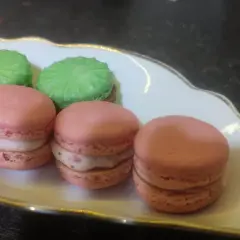 Trzy różowe i dwa zielone makaroniki na ozdobnej białej paterce.