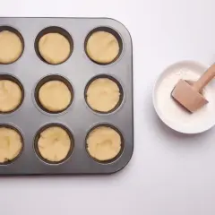 Forma z ciastem na mini tartaletki i miseczka z mąką i drewnianym narzędziem do wyciskania.
