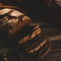 Pokrojony chleb ciemny, pachnący świeżością, leży obok miseczki z oliwkami.