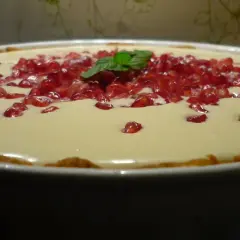 Pyszna tarta z kremem z białej czekolady, ozdobiona pestkami granatu i listkiem mięty.