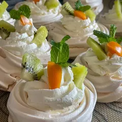 Słodkie gniazdka bezowe z bitą śmietaną, kiwi i pomarańczową dekoracją.