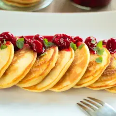 Puszyste pancakes na maślance, polane wiśniowym sosem i ozdobione listkami mięty. Idealne na słodkie śniadanie.