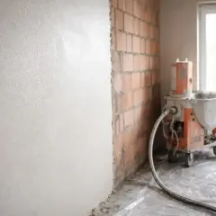 Maszyna tynkarska nakłada pierwsza warstwa tynku na ścianę z cegły.