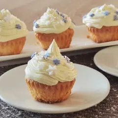 Pyszne muffinki z kremem w środku, ozdobione białym kremem i niebieskimi oraz białymi posypkami w kształcie gwiazdek i płatków śniegu.
