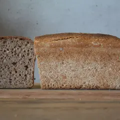 Chleb z mąki orkiszowej, jeden bochenek pokrojony, drugi w całości, na desce.