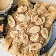 Naleśniki z bananami i czekoladową posypką, polane obficie kremową polewą z masła orzechowego.