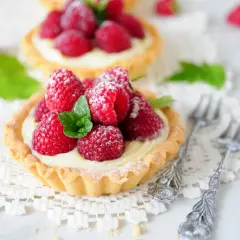 Malinowa chmurka w tartaletce, ozdobiona świeżymi malinami i listkiem mięty, posypana cukrem pudrem.
