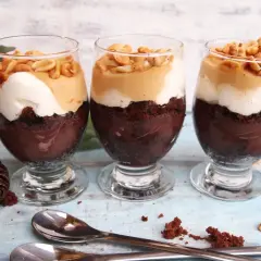 Trzy pucharki z deserem snickers: czekoladowy spód, krem, karmel i orzeszki.