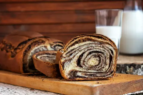 Pyszne drożdżowe z czekoladą, pokrojone na desce, obok szklanka mleka. Idealne na śniadanie.