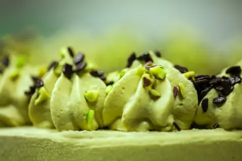 Delikatna beza z kremem pistacjowym, ozdobiona posiekanymi pistacjami i czekoladą.