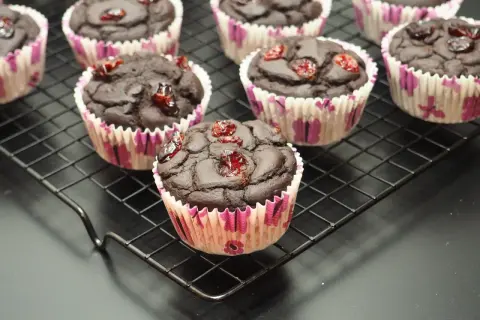 Czekoladowe muffinki z fasoli, ozdobione suszoną żurawiną, prezentują się apetycznie na czarnej kratce.