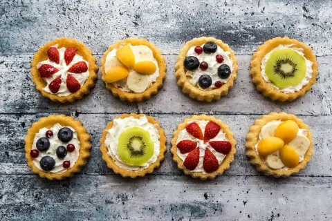Kolorowe tartaletki z owocami: truskawki, kiwi, borówki, maliny i morele na kremowym nadzieniu.