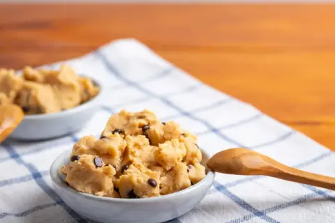 Masa na ciasteczka z kawałkami czekolady w miseczkach, gotowa do pieczenia. Obok drewniana łyżka.