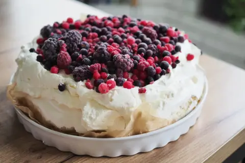 Beza pavlova z 10 białek, obficie udekorowana mrożonymi owocami leśnymi. Puszysta masa i kolorowe owoce tworzą apetyczny deser.