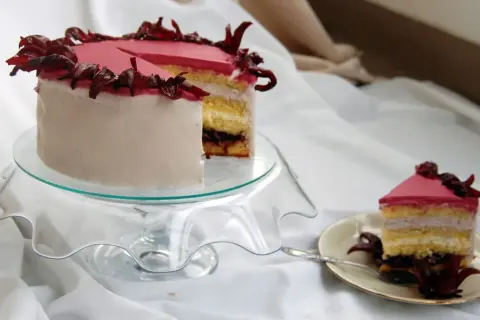 Różowy tort z kremem hibiskusowym, ozdobiony suszonymi kwiatami hibiskusa.