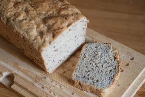 Chleb z lnem, świeżo upieczony, z jedną kromką obok, na drewnianej desce.