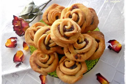 Urocze ciastka różyczki z dżemem, ułożone na zielonej paterze, ozdobione płatkami róży.