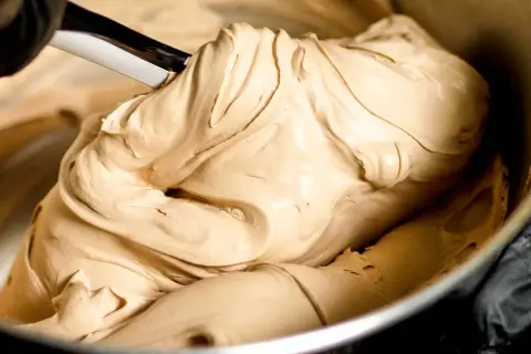 Gładka, kremowa masa o kolorze **salted caramel** jest mieszana łopatką w metalowej misce.