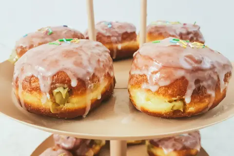 Pyszne pączki pistacjowe z lukrem i kolorową posypką, ułożone na paterze.