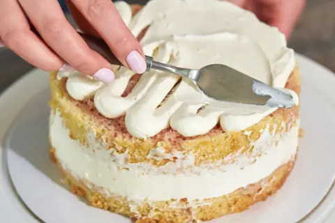 Ręce dekorują biszkoptowy tort, rozprowadzając puszyste kremy. Idealne kremy do ciasta biszkoptowego tworzą piękne wzory.