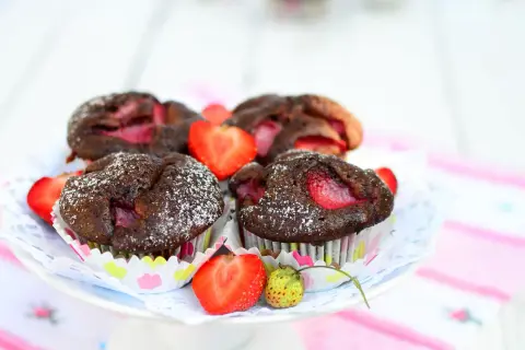 Pyszne muffiny czekoladowe z truskawkami, posypane cukrem pudrem, prezentują się apetycznie na talerzyku.