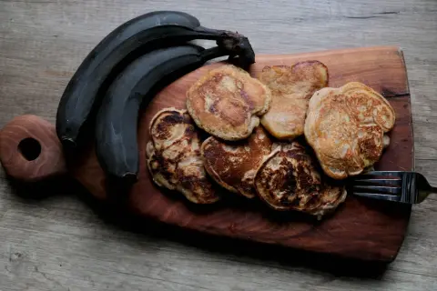 Placki bananowe z masłem orzechowym, obok ciemnych bananów, na drewnianej desce. Idealne na śniadanie.