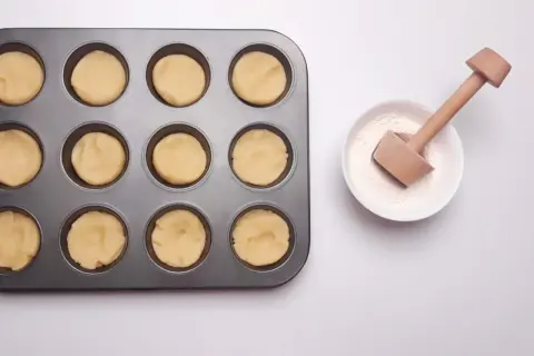 Forma z ciastem na mini tartaletki i miseczka z mąką i drewnianym narzędziem do wyciskania.
