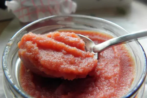 Łyżeczka zanurzona w słoiku z gęstym, różowym curd wiśniowym. Idealny dodatek do deserów.