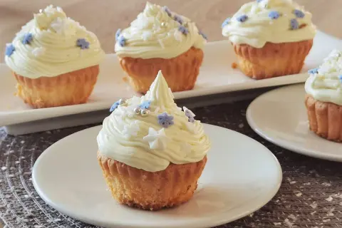 Pyszne muffinki z kremem w środku, ozdobione białym kremem i niebieskimi oraz białymi posypkami w kształcie gwiazdek i płatków śniegu.