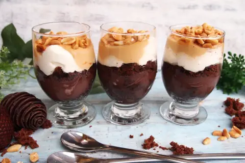 Trzy pucharki z deserem snickers: czekoladowy spód, krem, karmel i orzeszki.