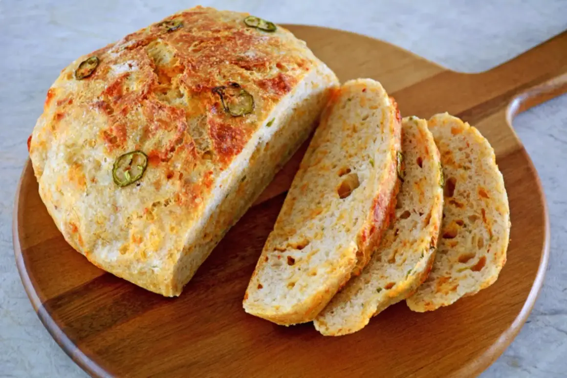 Chleb z serem i papryczką jalapeno, pokrojony na kromki, leży na drewnianej desce.