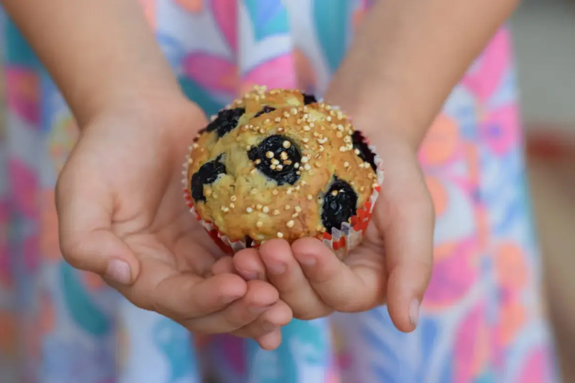 Dziecko trzyma w dłoniach pyszne muffinki z borówkami mrożonymi, posypane chrupiącym ziarnem.