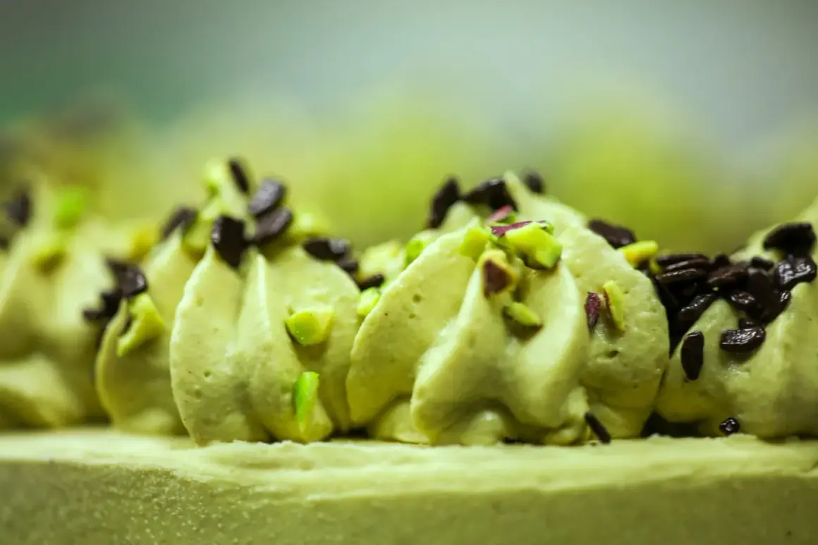 Delikatna beza z kremem pistacjowym, ozdobiona posiekanymi pistacjami i czekoladą.