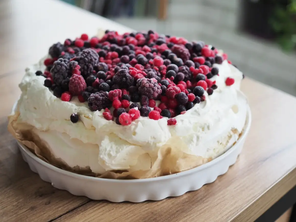 Beza pavlova z 10 białek, obficie udekorowana mrożonymi owocami leśnymi. Puszysta masa i kolorowe owoce tworzą apetyczny deser.