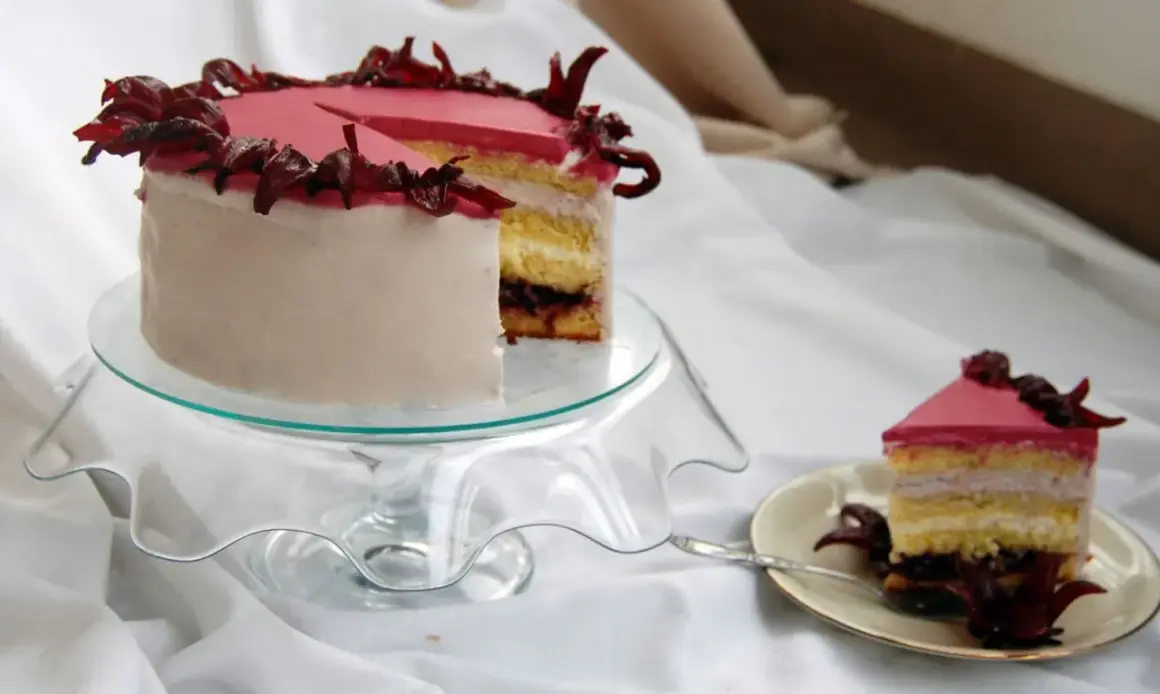 Różowy tort z kremem hibiskusowym, ozdobiony suszonymi kwiatami hibiskusa.