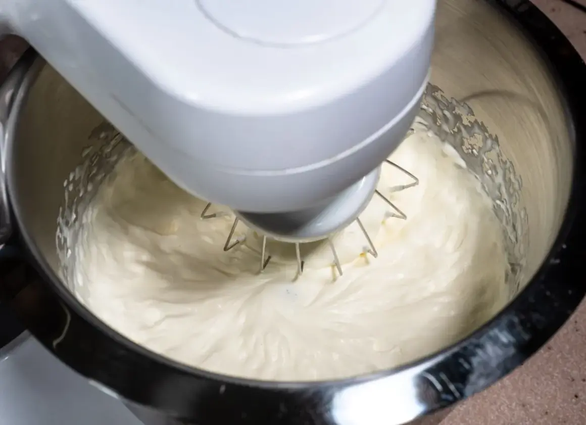 Mieszadło robota kuchennego ubija puszysty krem z ricotty do ciasta.