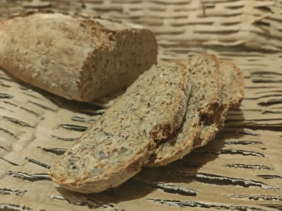 Wilgotny chleb orkiszowy, pokrojony w kromki, z widocznymi ziarnami. Idealny na śniadanie.