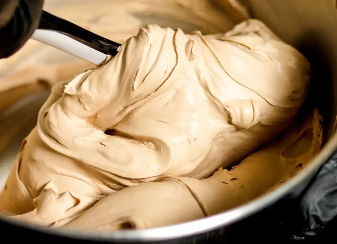 Gładka, kremowa masa o kolorze **salted caramel** jest mieszana łopatką w metalowej misce.