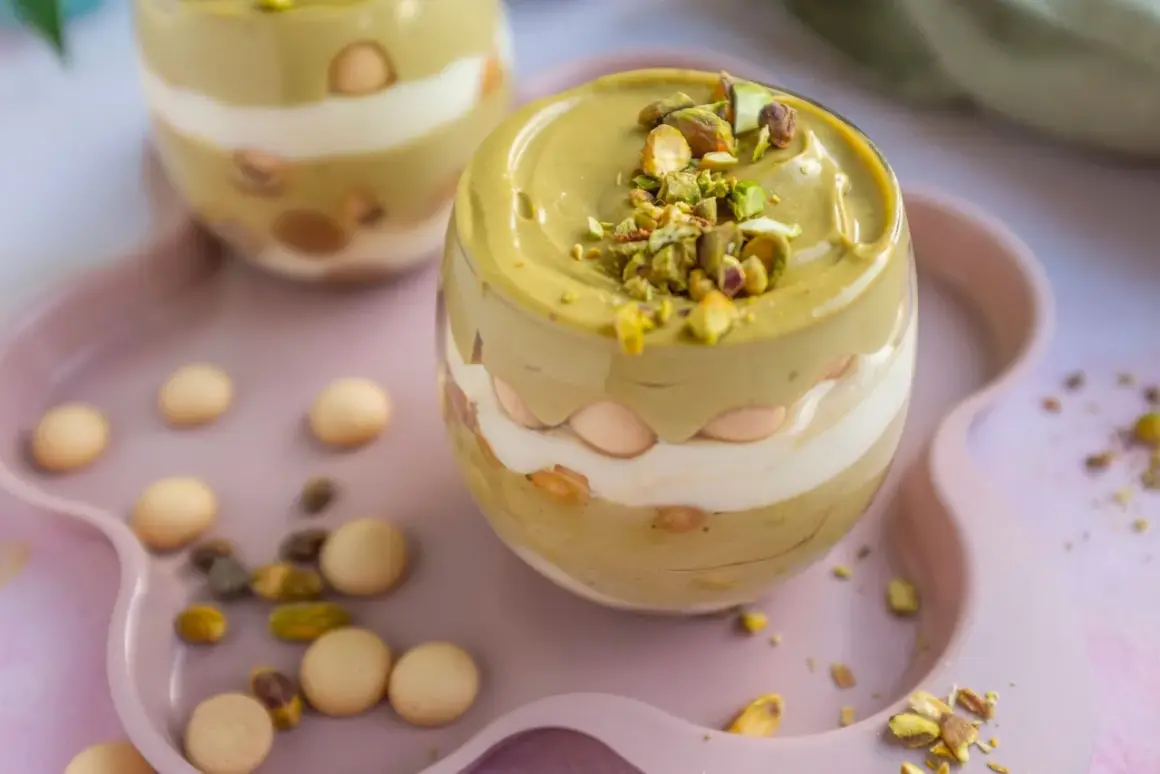 Pyszne tiramisu pistacjowe w szklance, przełożone kremem i biszkoptami, posypane posiekanymi pistacjami.